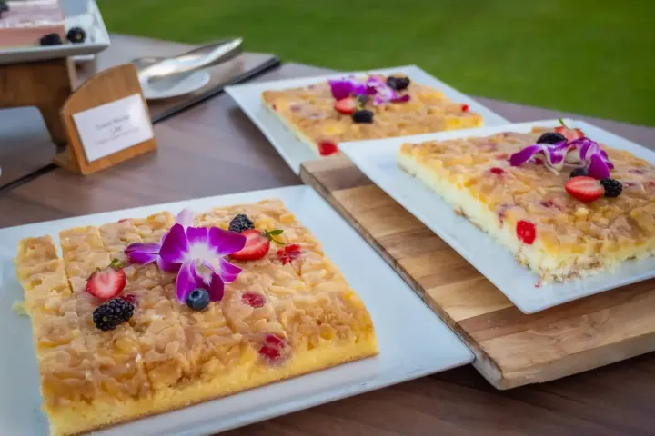 Square cakes with berries and purple flowers on plates.