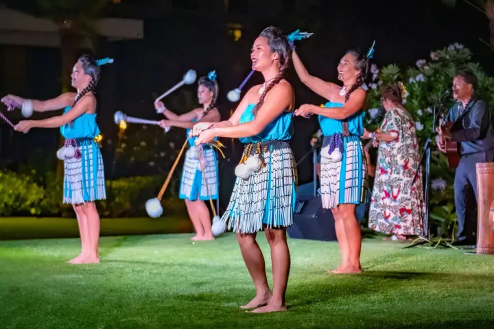 Women in traditional attire perform a cultural dance outdoors at night.