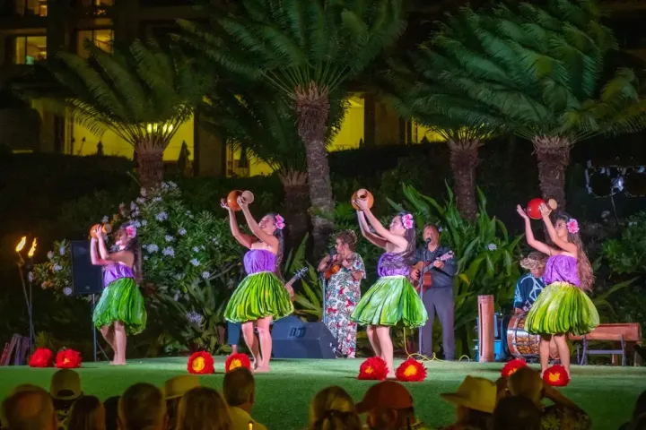 Hula dancers in green skirts perform on stage with musicians at night.